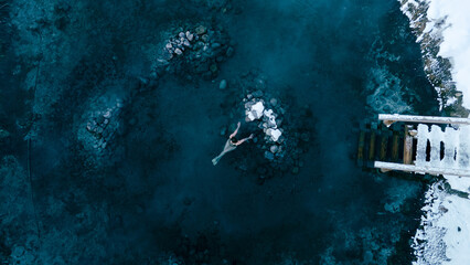 Aerial view of a lone woman relaxing in a stunning thermal spring surrounded by snowy landscapes in...