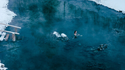 Aerial view of a lone woman relaxing in a stunning thermal spring surrounded by snowy landscapes in Northern Buryatia. Winter serenity and natural beauty.