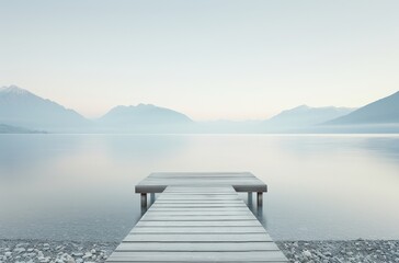 Naklejka premium Serene lake view with a wooden dock extending into calm waters, surrounded by mountains under a gentle, overcast sky.