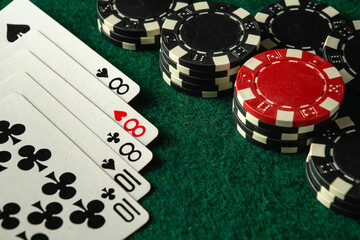 A close-up shot shows a set of playing cards showing full house or full boat next to various poker chips on a green felt table. The excitement of the game is palpable