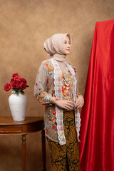 Elegant Muslim woman in traditional kebaya outfit with batik, posing gracefully in a classic indoor setting