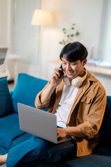 Smiling asian freelancer working from home, using laptop and talking on phone