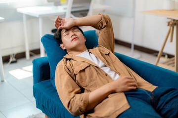 Obraz premium Exhausted asian man resting on sofa after working remotely from home office