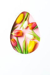 Egg-shaped cutout filled with colorful tulips on a pink background. Festive floral concept for Easter and spring.