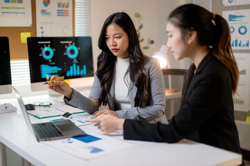 Professional women collaborating, reviewing financial data on laptop and calculator, strategizing business performance in modern office workspace