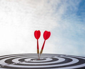 Two red darts hitting the bullseye on a target board under a bright sky. Symbol of accuracy,...