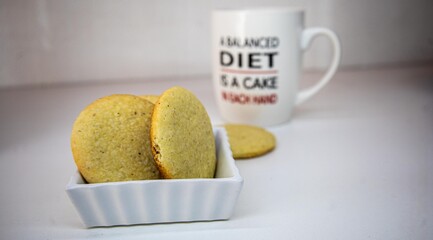 A white ceramic mug with a humorous quote about dieting sits behind a plate of golden, homemade cookies.