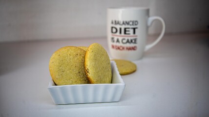 A white ceramic mug with a humorous quote about dieting sits behind a plate of golden, homemade cookies.