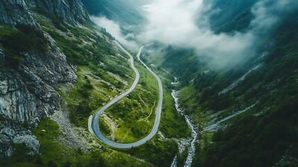 Aerial view of a winding mountain road cutting through lush greenery, with mist hovering above