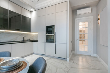 Stylish kitchen design with a white kitchen set. Dining table, upholstered chairs. A white door with glass windows.