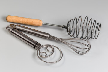 Different stainless steel hand kitchen whisks on a gray background