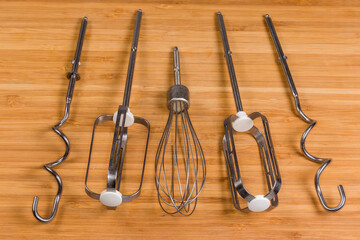 Different whisk-attachments for kitchen mixer on wooden cutting board