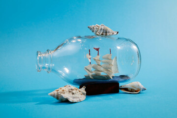 Ship in a bottle with seashells on light blue background