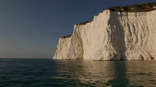Majestic White Cliffs of Dover rising dramatically against calm blue sea waters, showcasing iconic chalky coastline under clear summer skies in Kent, United Kingdom
