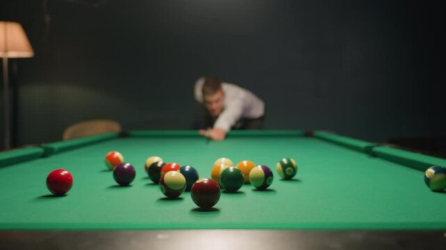 Blurred figure in light shirt and dark trousers leans over green pool table, gripping cue stick with deep concentration. Eyes locked on balls, posture steady. Dim lighting casts