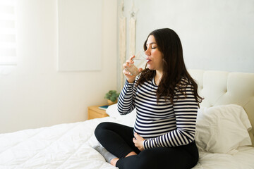 Pregnant woman drinking water, resting on bed, staying hydrated during pregnancy