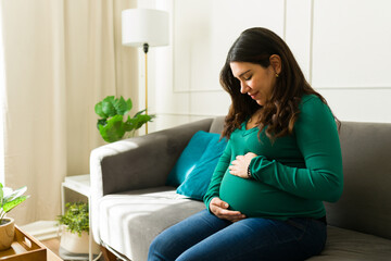 Pregnant woman resting on sofa, gently cradling growing belly in serene home environment