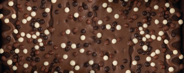 Chocolate brownie cake texture background sprinkled with white and dark balls, brounie banner