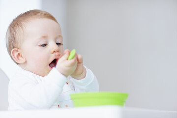 Baby, eating food and nutrition in home, hungry and learning motor skills for child development. Boy, high chair and spoon for cognitive growth, space and healthy meal for infant diet or wellness