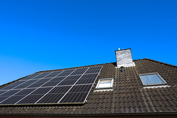 Fototapeta premium Photovoltaic solar panels providing green energy on a roof against blue sky