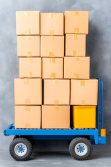 A blue hand truck carries a stack of cardboard boxes and a yellow container