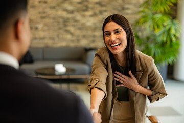 Businesswoman shaking hands with client and smiling cheerfully in meeting room
