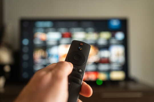 A person holds a remote in front of a vibrant TV screen, ready to browse and enjoy shows