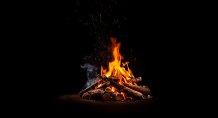 Vibrant flames rise from a neatly stacked bonfire, casting a warm glow in the dark night as embers float upwards.