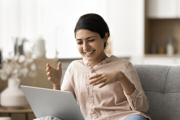 Funny virtual conversation. Cheerful laughing young girl relax on sofa at living room on weekend...