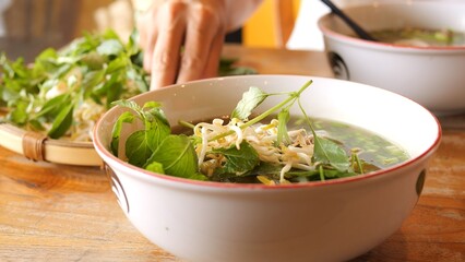 Vietnamese pho soup with aromatic broth rice noodles and fresh herbs Culinary process of adding basil mint and lime to enhance flavors showcasing cultural tradition and healthy dining experience