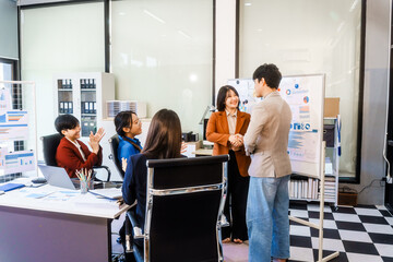 Five young Asian professionals collaborate at startup business meeting, working at desk with laptops and financial charts. They discuss strategy, funding, innovation, teamwork and problem solving.