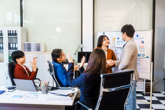Five young Asian professionals collaborate at startup business meeting, working at desk with laptops and financial charts. They discuss strategy, funding, innovation, teamwork and problem solving.