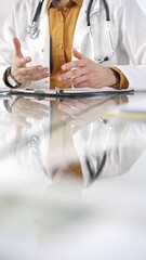 Unknown male doctor wearing a stethoscope, yellow shirt under a lab coat is gesturing with hands overs a glass desk with a laptop in clinic office. Medicine concept