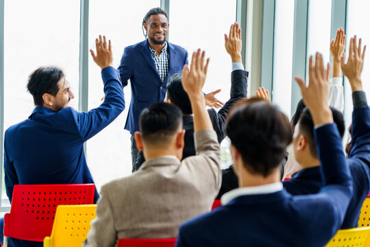 african american business man standing and talking in font of group of diversity business people in meeting at seminar listener raising hand to ask question. black speaker giving lecture