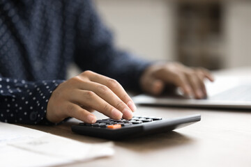 Fototapeta premium Economy and finance planning. Cropped close up shot young businesswoman do financial paperwork. Focus on female hand counting on calculator. Paying bills taxes budgeting work accounting audit concept