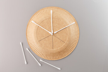 a brown paper plate with three cotton swabs arranged on it, there are three more cotton swabs lying...