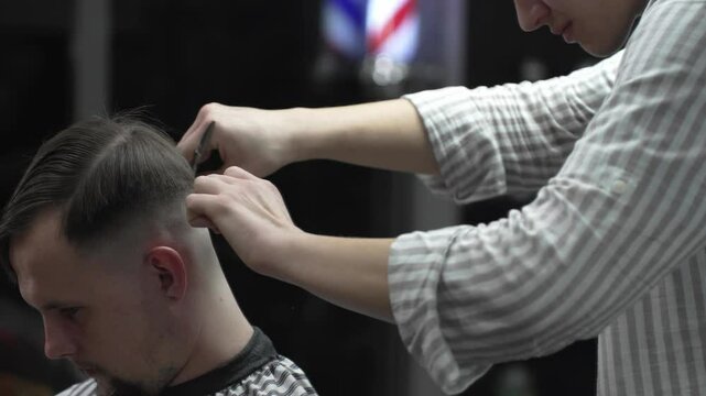 Professional barber carefully combing client's hair, preparing precise hairstyle with expert grooming techniques in modern barbershop setting