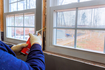 Contractor is sealing gaps around window frame with insulation foam during home renovation project