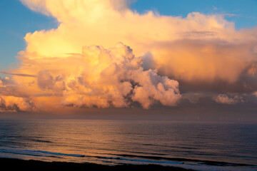Dramatic cloudscape over the sea at sunrise with clouds changing from white to orange in front of a blue sky