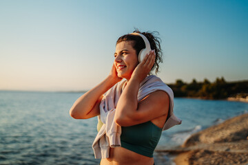 Young caucasian woman put on headphones and stretch before run on beach at sunset