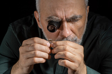 Jewelry appraiser examines a gold ring evaluating large diamond looking through magnifying glass...