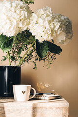 Home office desk workspace with blank paper clipboard, blue hydrangea flower bouquet, cup of coffee and keyboard on white wooden background.
Romantic background with space for text.
