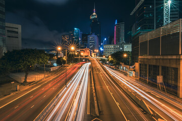 A mesmerizing long exposure photograph of Hong Kong's vibrant cityscape at night. Towering skyscrapers pierce the inky sky, their illuminated windows creating a dazzling tapestry of light. 