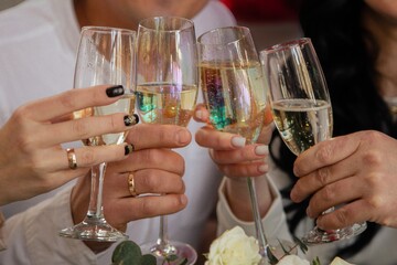 People raise glasses of champagne in a festive atmosphere. Hands with manicure, wedding rings and accessories are visible. Warm and joyful atmosphere, a symbol of celebration, wedding 