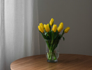 Fresh yellow tulips in a glass vase on a round wooden table