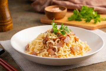 Instant noodle carbonara sauce topped with crispy bacon and parmesan cheese in white plate.