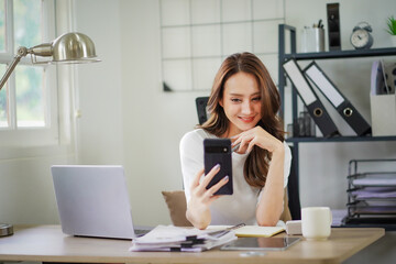 A woman is sitting at a desk with a laptop and a cell phone