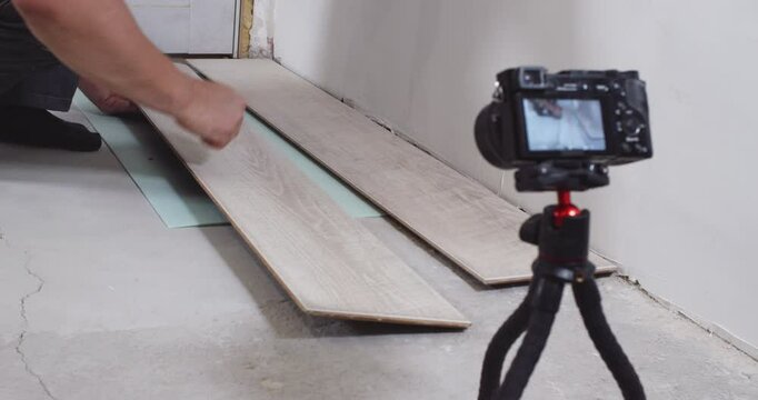Construction worker squatting and holding a laminate plank, showcasing the material in front of the camera. Focus on the plank highlights its texture and design for flooring projects