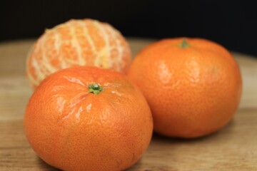 Fresh whole and peeled tangerines on a wooden surface.