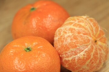 A group of ripe tangerines, some peeled, on a wooden table.